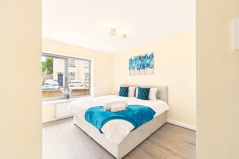 Bright bedroom with double bed, blue bedding, large window overlooking garden, and artwork