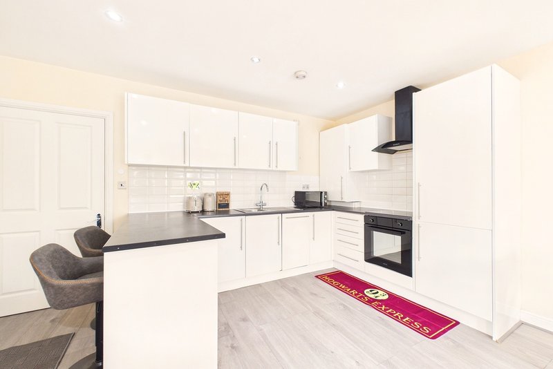 Modern white kitchen with island, black worktops, integrated oven and red floor mat