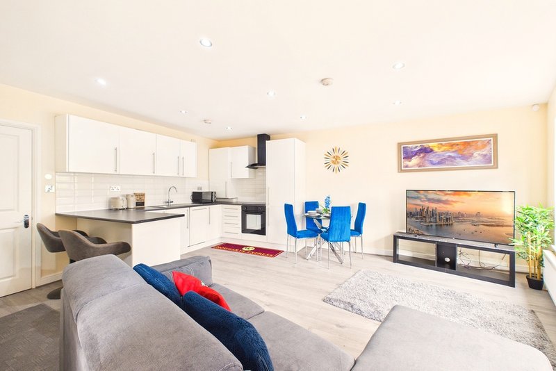Open-plan living area with kitchen, sofa, dining table and chairs, wall art and plants
