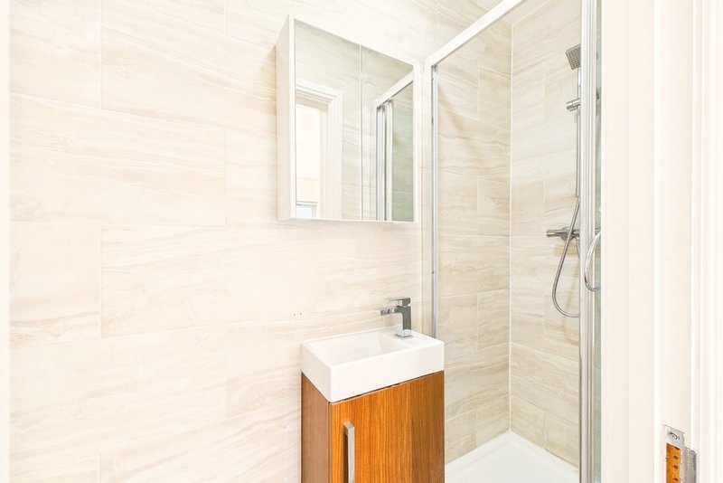 Modern bathroom with wooden vanity, white sink, mirror, and enclosed shower cubicle
