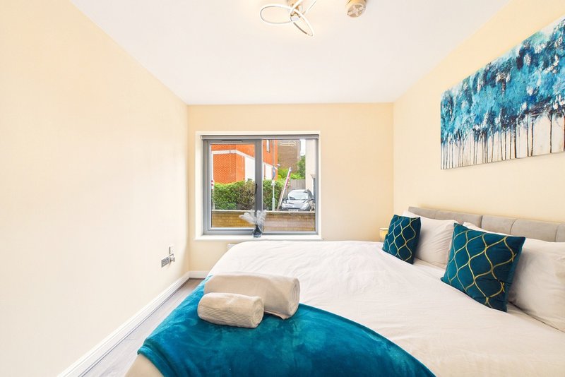 Bright bedroom with double bed, teal bedding, decorative pillows and window overlooking garden