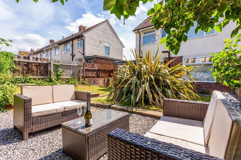 Garden patio area with rattan furniture, cushions, potted plants and gravel, adjacent to brick house