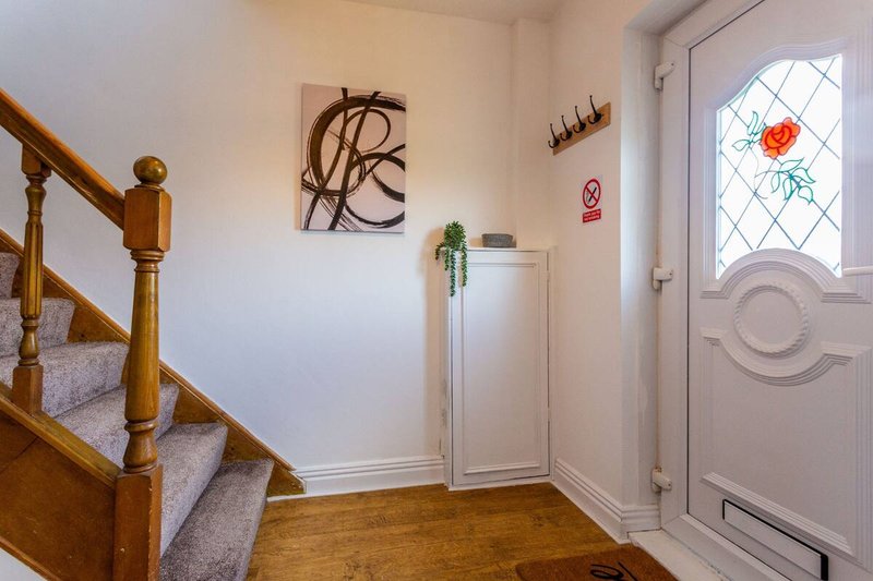 Hallway with wooden staircase, white walls, abstract artwork, and front door with decorative glass panel