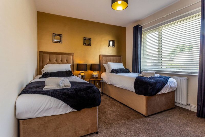 Twin bedroom with two single beds, bedside tables, yellow accent wall and window with blinds