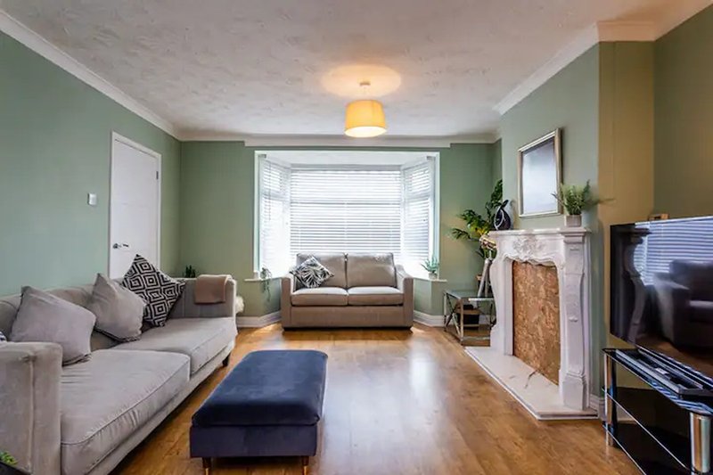 Spacious living room with green walls, sofas, fireplace, bay window and wooden flooring