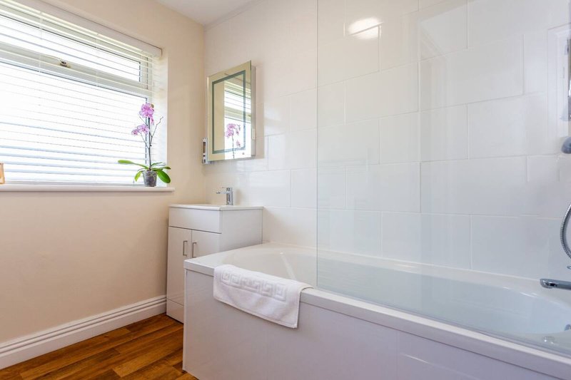 Clean modern bathroom with white bathtub, sink vanity, mirror, and wooden floor