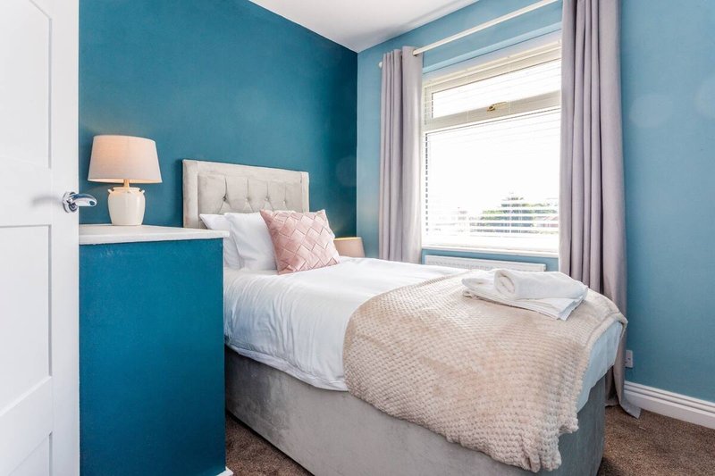 Bright bedroom with teal walls, double bed, white headboard, and large window with grey curtains