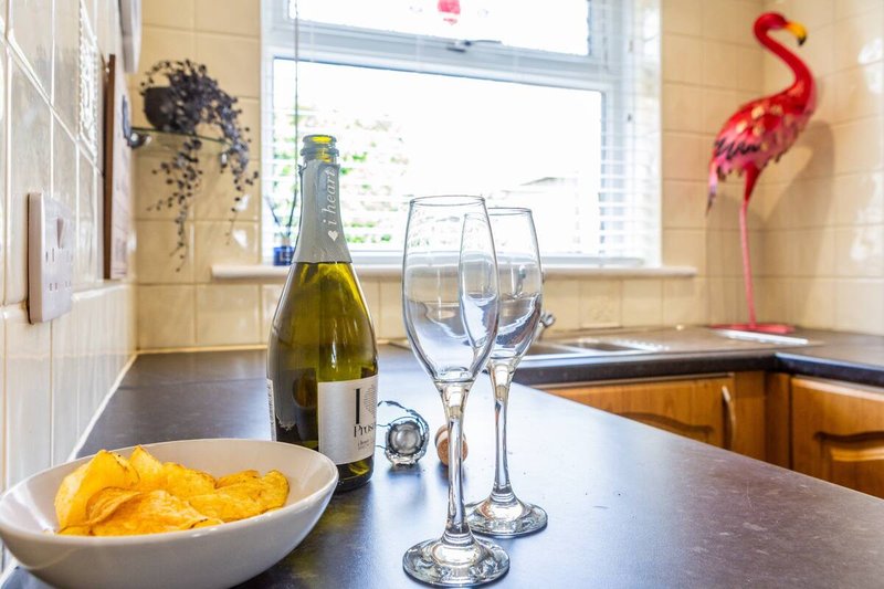 Kitchen counter with wine bottle, glasses, bowl of crisps and decorative wall hangings