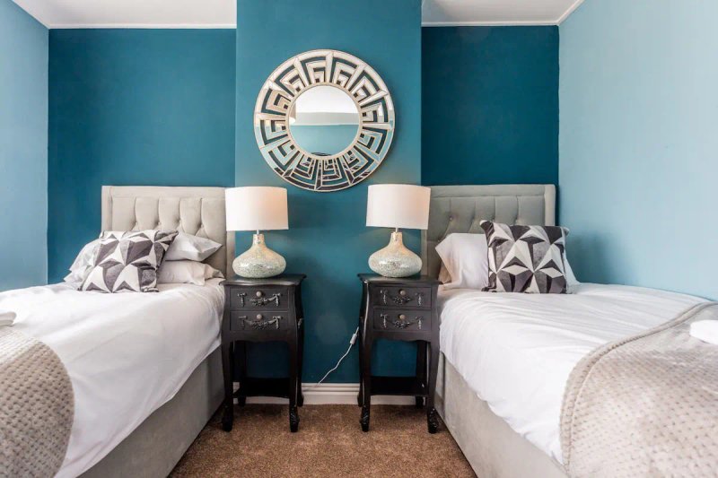 Twin bedroom with teal accent wall, matching beds, bedside tables, lamps and decorative mirror