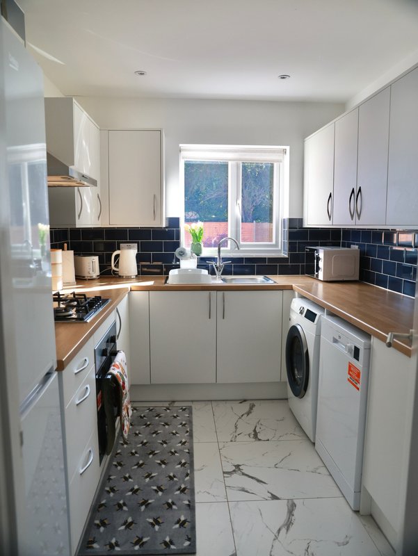 Modern kitchen with white cabinetry, black tile backsplash, wooden worktops, and integrated appliances