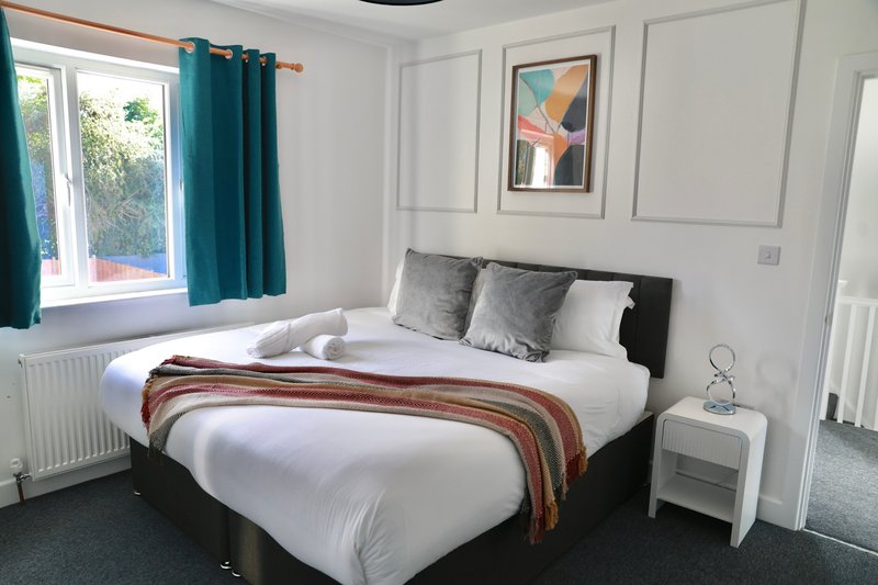 Bright bedroom with double bed, black headboard, white bedding, teal curtains and bedside table