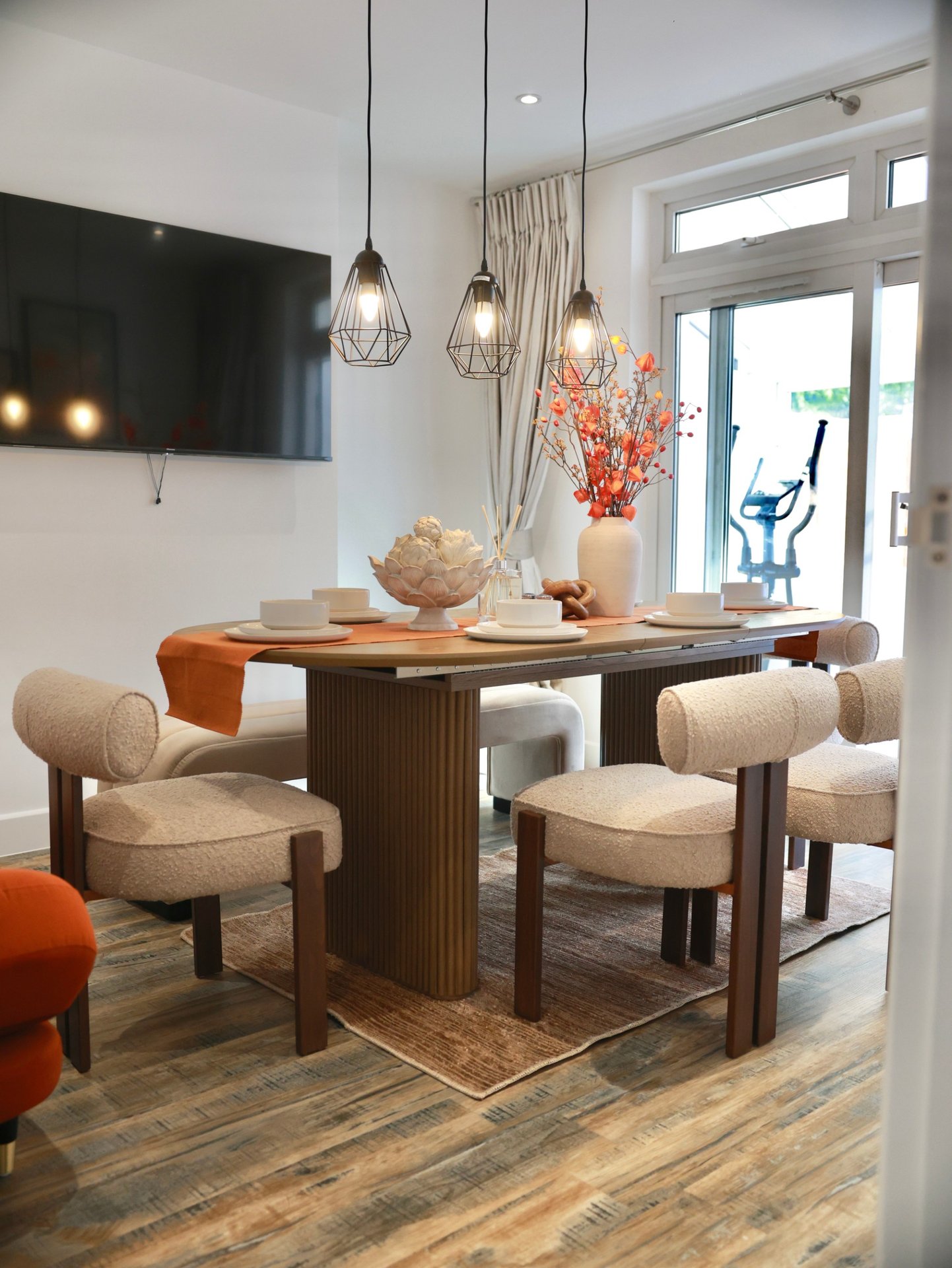 Modern dining area with wooden table, beige upholstered chairs, pendant lights, and glass doors