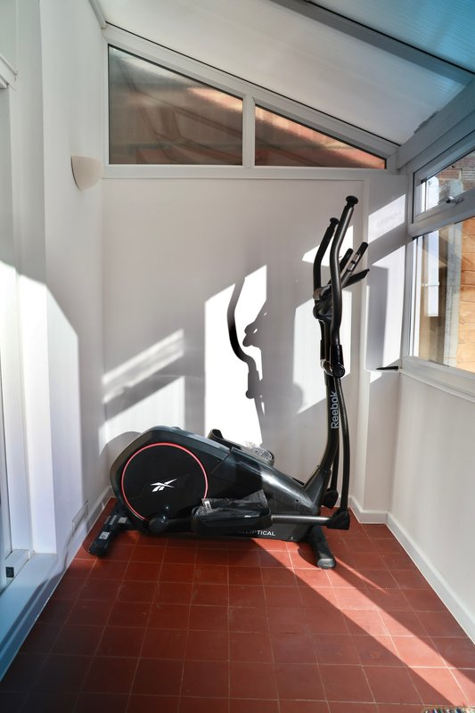 Home gym corner with exercise bike and weights on terracotta floor
