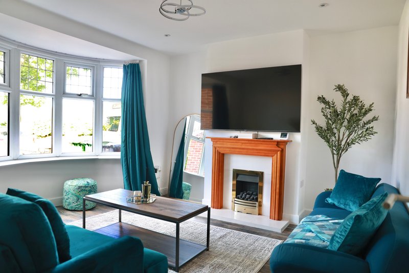 Bright living room with teal sofas, fireplace with TV, large windows and potted plant