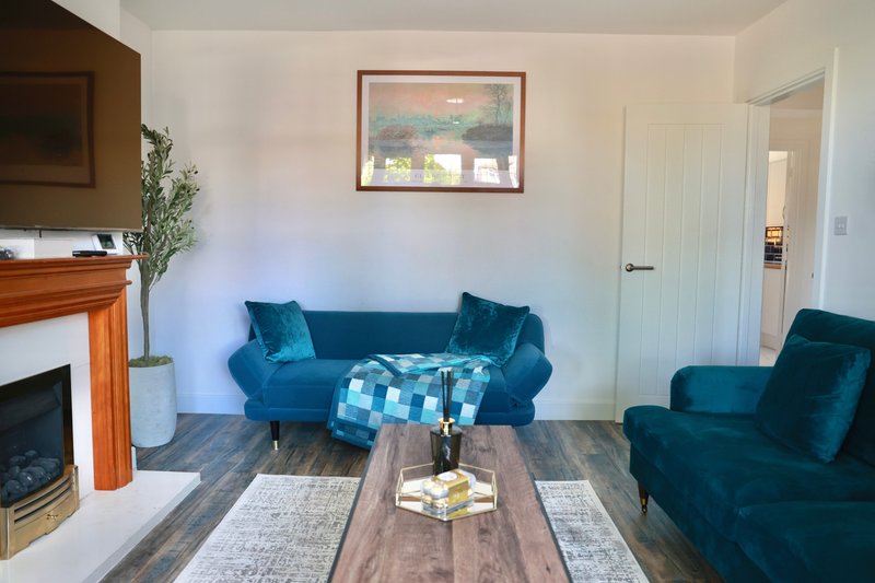 Living room with blue velvet sofa, fireplace, wooden coffee table and armchair