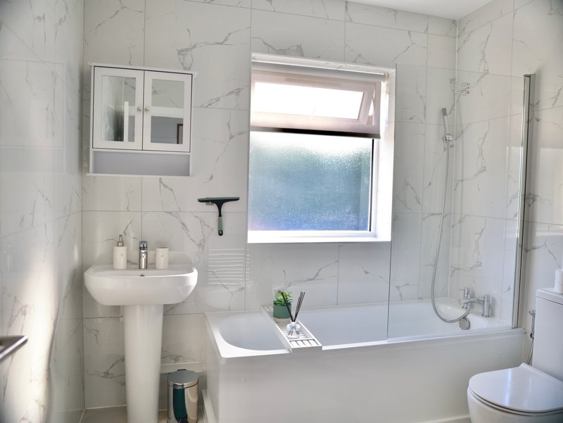 Modern bathroom with marble tiles, pedestal sink, bathtub, and window with frosted glass