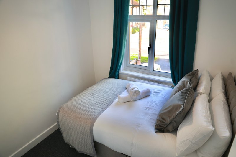 Bright bedroom with double bed, white bedding, green curtains and garden view