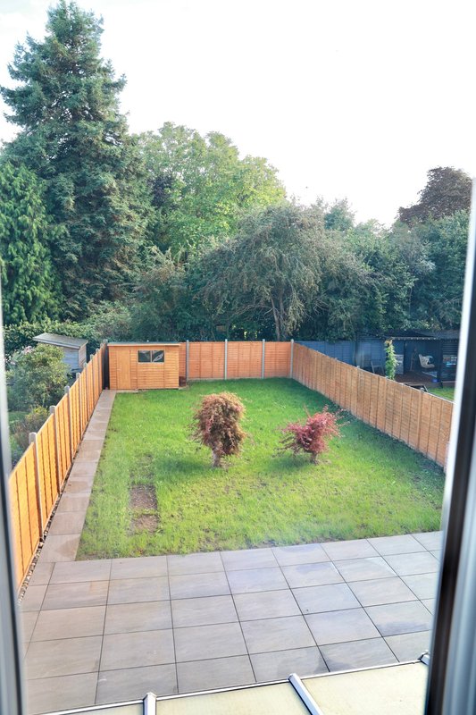Enclosed garden with paved patio, lawn, wooden fencing and mature trees