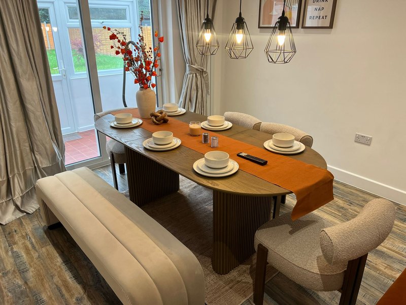 Modern dining room with oval wooden table, place settings, pendant lights and garden view