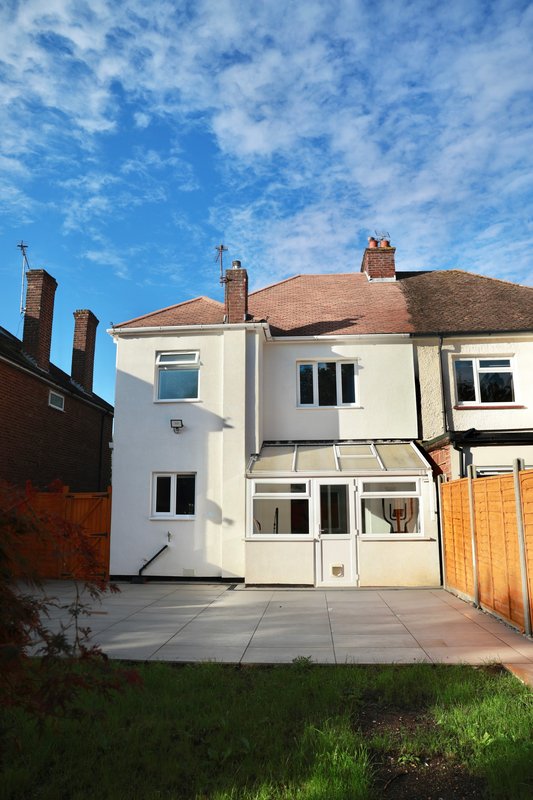 Two-storey semi-detached house with cream render, patio, and wooden garden fence