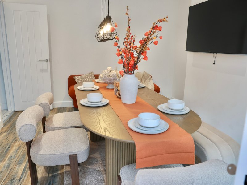 Modern dining room with wooden table, upholstered chairs, place settings, and floral centerpiece