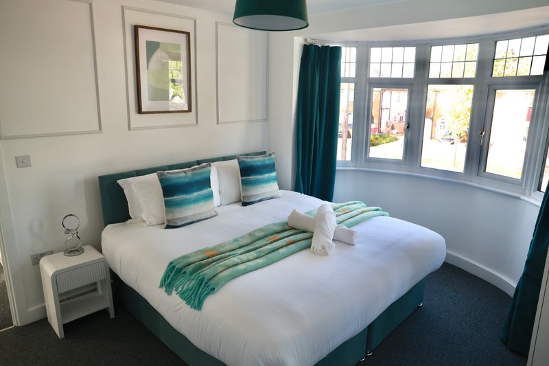 Bright bedroom with double bed, teal headboard, bay windows and garden views