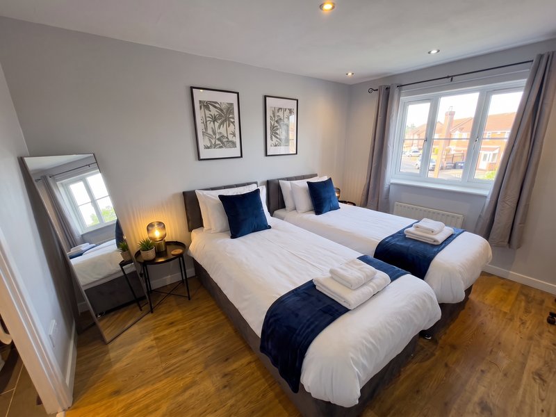 Modern twin bedroom with two single beds, wooden floor, mirror, and large window