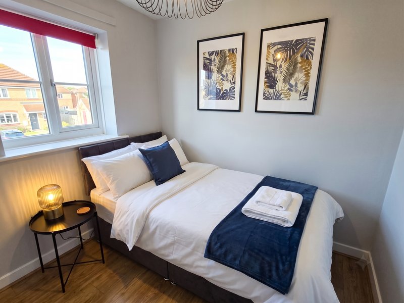 Bright bedroom with double bed, white bedding, navy throw, bedside lamp and framed botanical prints