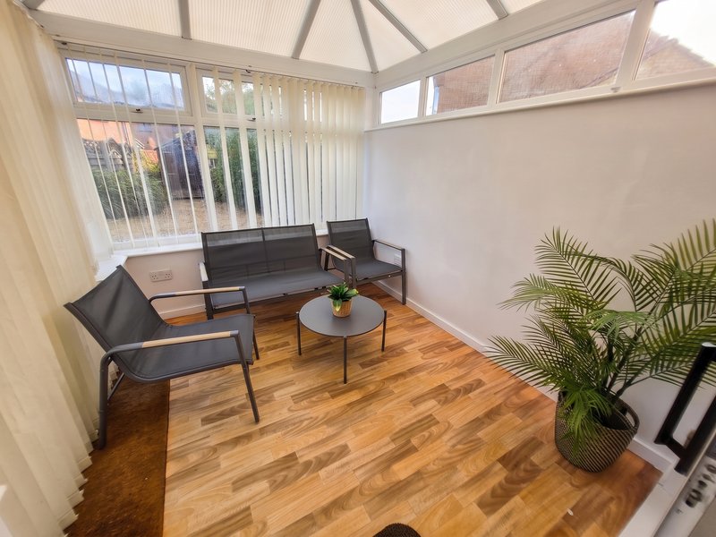 Bright conservatory with black chairs, wooden floor, potted plant and glass roof panels