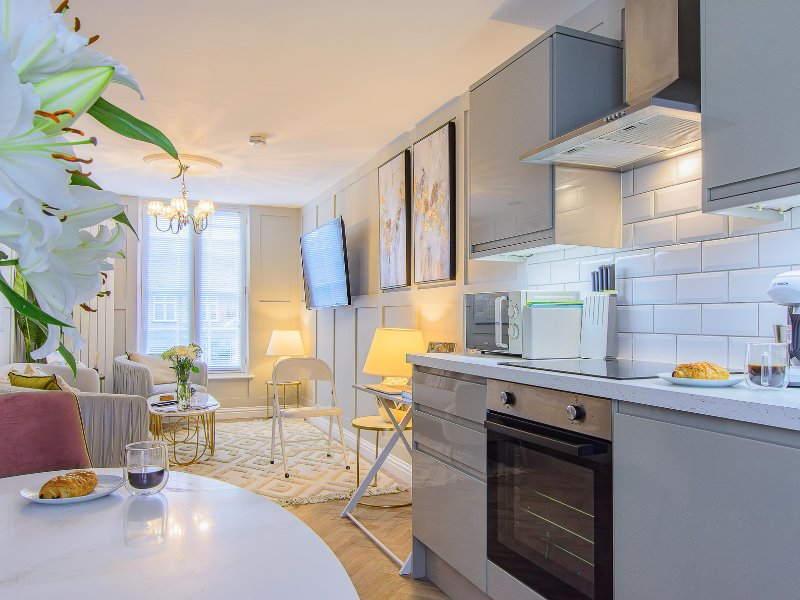 Modern open-plan kitchen and living area with white cabinetry, dining table, and seating by windows