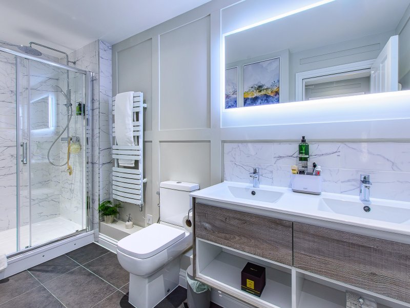 Modern bathroom with double sink, walk-in shower, toilet, and illuminated mirror