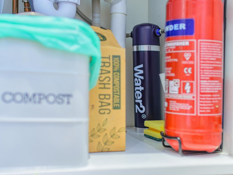 Kitchen shelf with compost bin, trash bag, water bottle and cleaning supplies