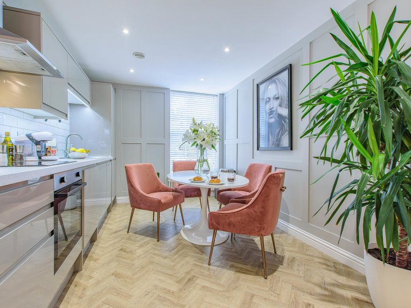 Modern open-plan kitchen and dining area with cream cabinets, round table, coral chairs and potted plant
