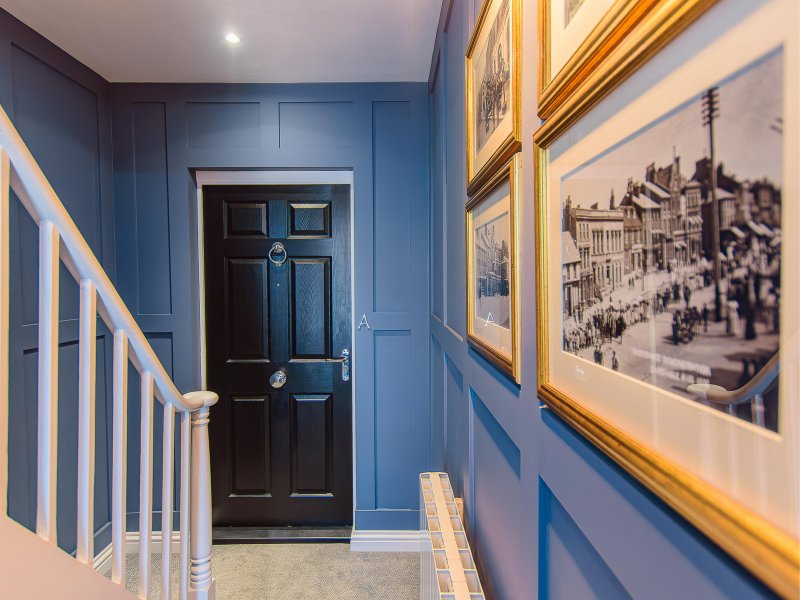 Blue hallway with black door, white stair railing, and framed black-and-white photographs