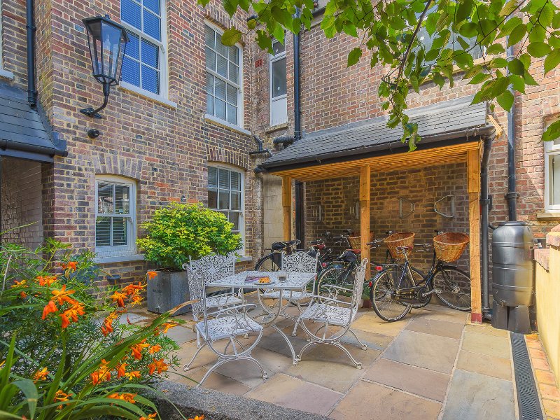 Brick courtyard with patio seating, bicycles, flowering plants and wooden pergola extension