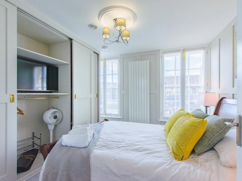 Bright modern bedroom with double bed, yellow and grey cushions, built-in wardrobe and large windows