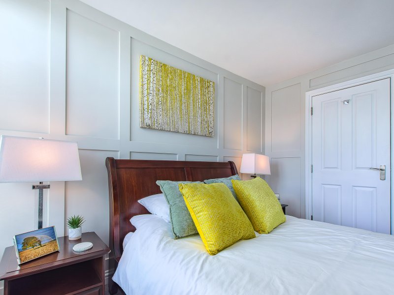 Modern bedroom with wooden bed frame, yellow and green cushions, white bedding, and wall art