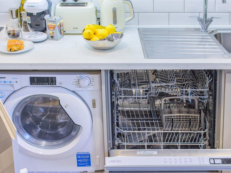 Modern kitchen with white countertop, washing machine, dishwasher, sink, and small appliances