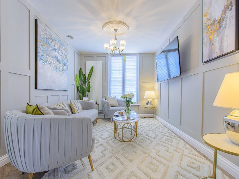Bright modern living room with gray upholstered sofa, armchair, geometric rug, and wall art