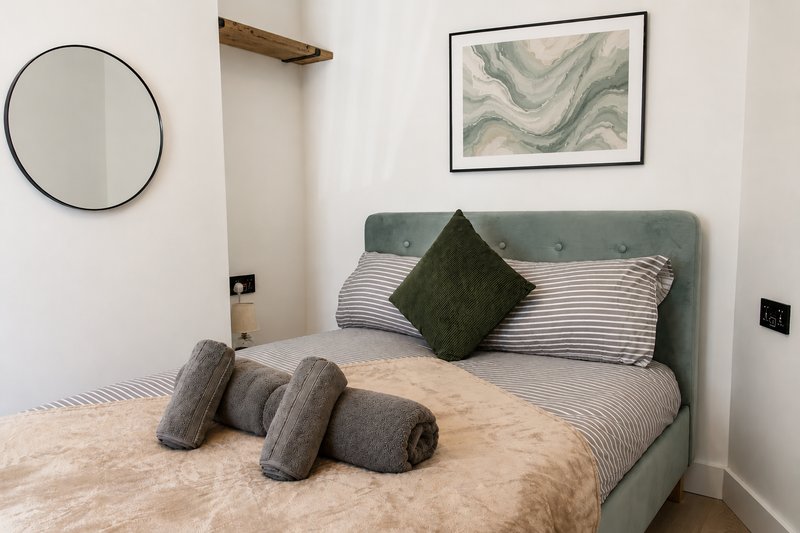 Modern bedroom with grey upholstered bed, striped pillows, decorative cushions and circular mirror on wall