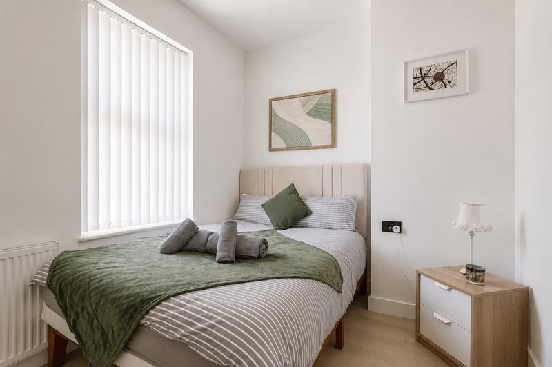 Modern bedroom with double bed, green bedding, wooden nightstand and vertical blinds