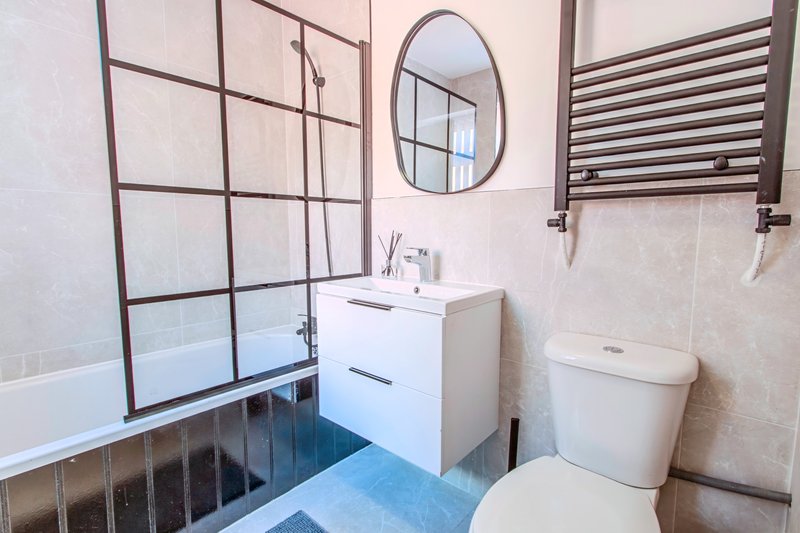 Modern bathroom with bathtub, white vanity, toilet, oval mirror and heated towel rail
