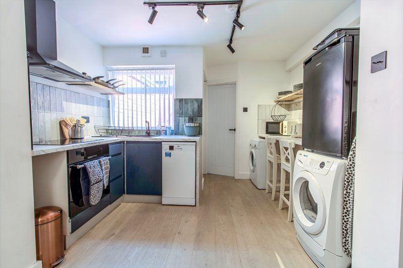Open-plan kitchen and utility room with dark cabinetry, appliances, washing machine and vertical blinds