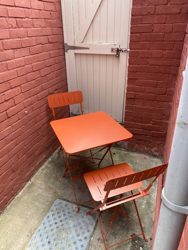 Small brick courtyard with orange table, chairs, and white door