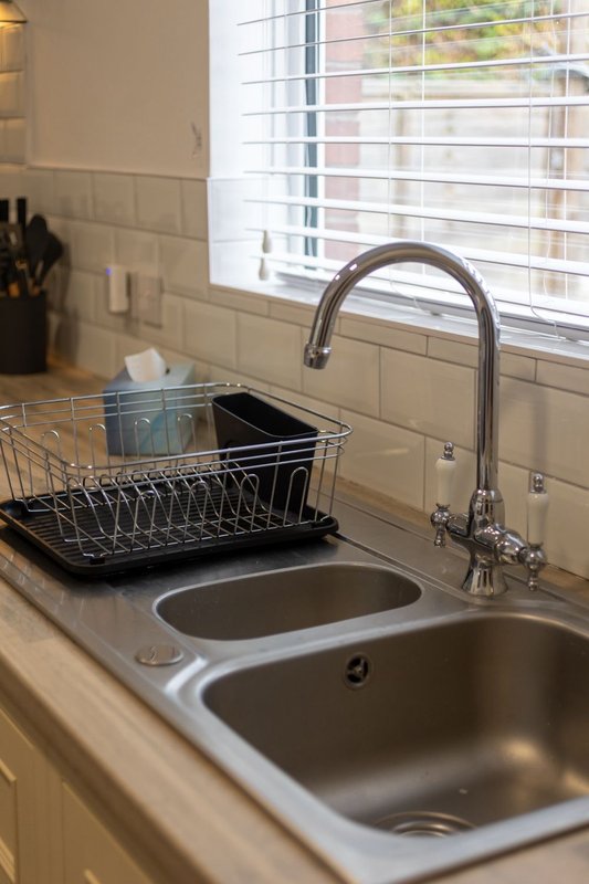 Kitchen sink with dual basins, chrome faucet, dish rack and window with blinds