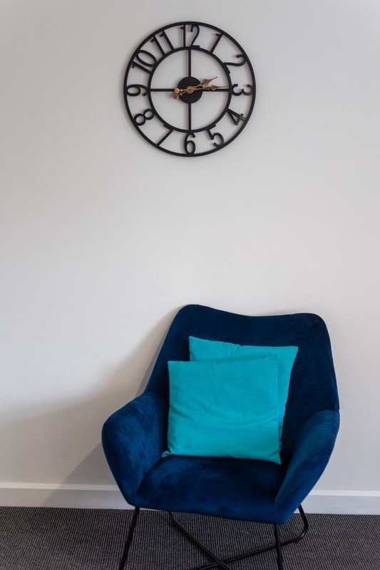 Modern bedroom chair with navy upholstery and turquoise cushion, wall clock above