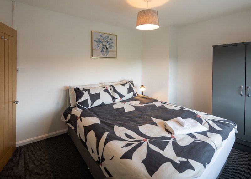 Bedroom with double bed, patterned duvet, pendant light, and wooden door