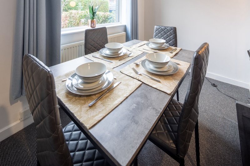 Dining table set for four with place settings, grey quilted chairs, and large window