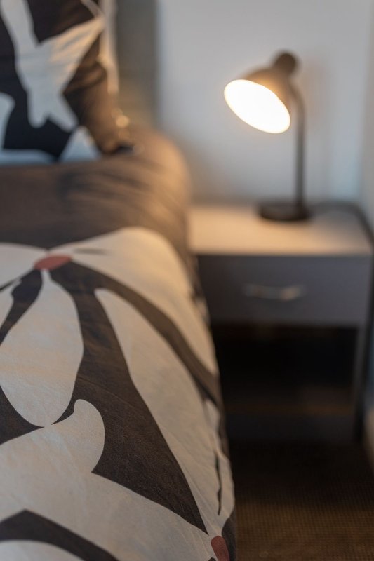 Bedroom detail with patterned bedding, desk lamp, and wooden nightstand