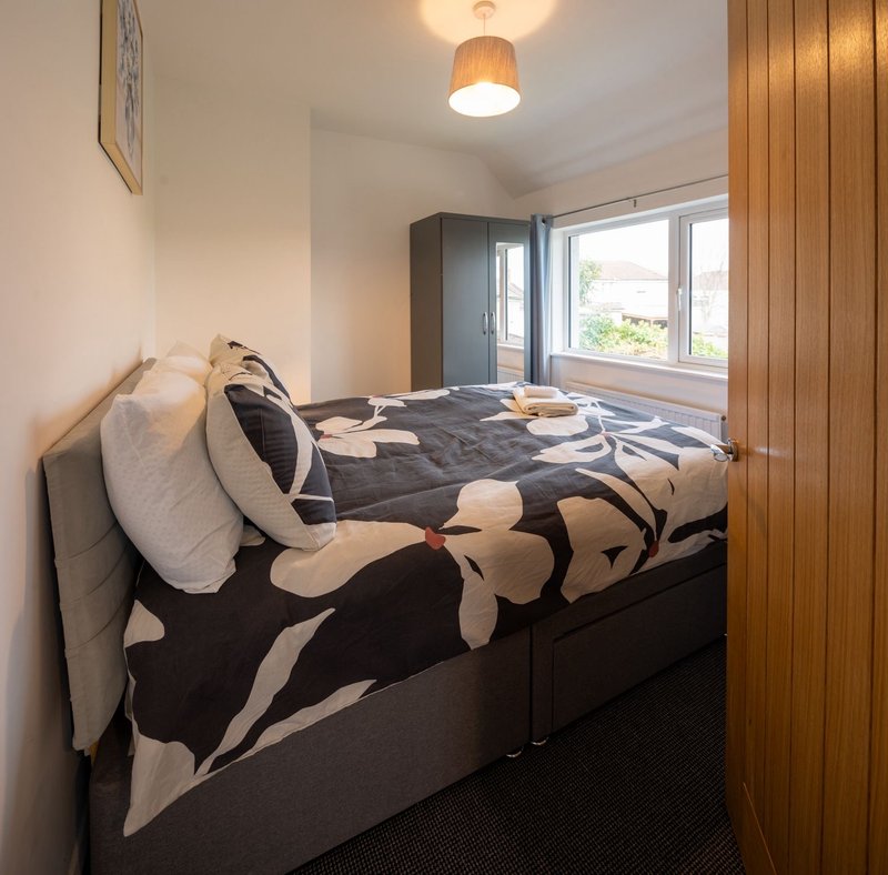 Compact bedroom with double bed, patterned duvet, pillows, wooden accent wall and window